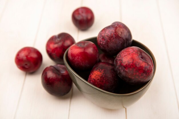 Vista superior de pluots de piel rojo oscuro en un recipiente con pluots aislado en una superficie de madera beige