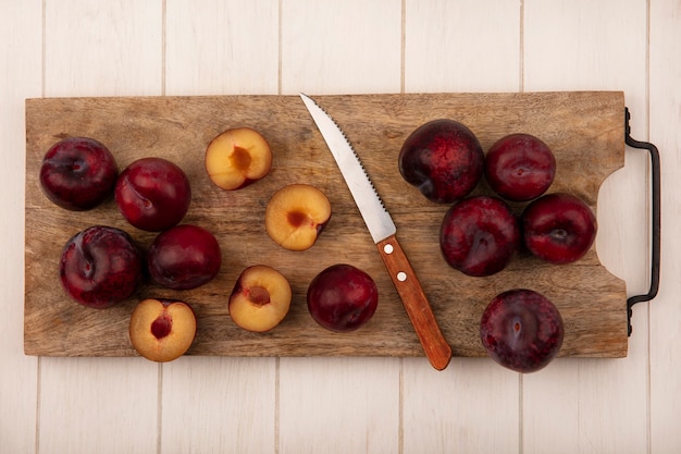 Vista superior de pluots rojo oscuro y dulce en una tabla de cocina de madera con cuchillo sobre un fondo de madera beige