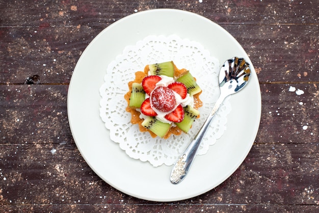 Una vista superior poco delicioso pastel con crema dentro de la placa con fresas frescas y kiwis en el fondo oscuro galleta bizcocho fruta