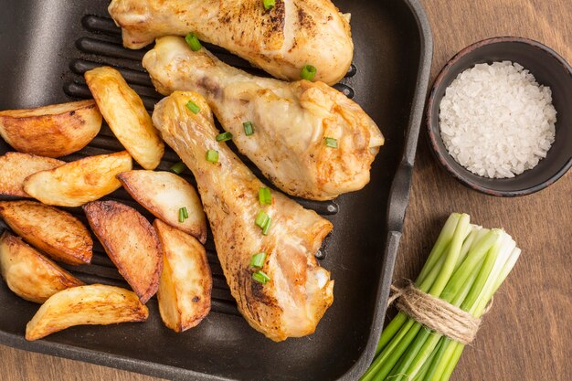 Vista superior de pollo al horno y gajos en sartén con sal y cebollas verdes
