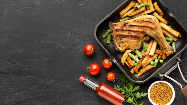 Vista superior de pollo al horno y patatas en una sartén con tomates y espacio de copia