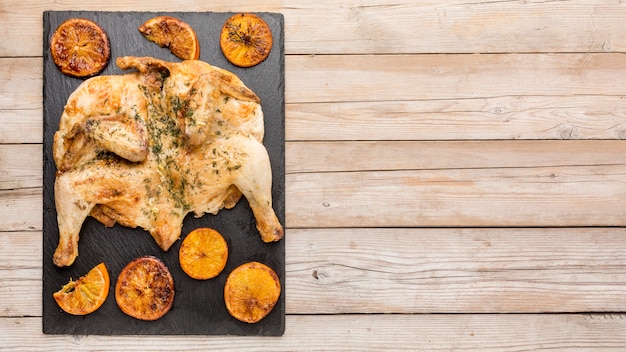 Vista superior de pollo al horno con rodajas de naranja y espacio de copia