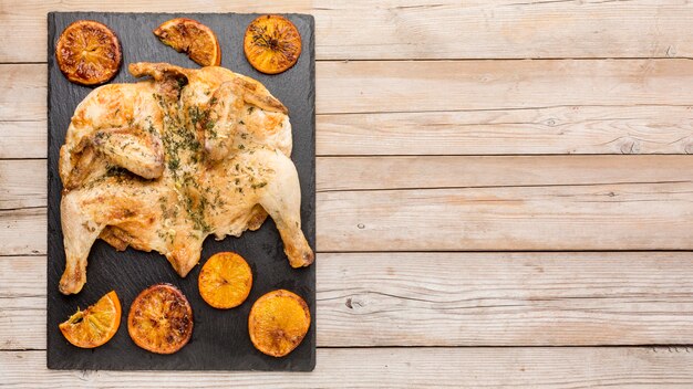 Vista superior de pollo al horno con rodajas de naranja y espacio de copia