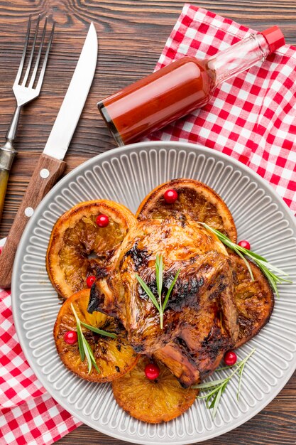 Vista superior de pollo al horno y rodajas de naranja en un plato con cubiertos y salsa