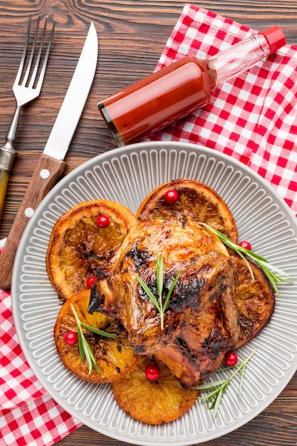 Vista superior de pollo al horno y rodajas de naranja en un plato con cubiertos y salsa