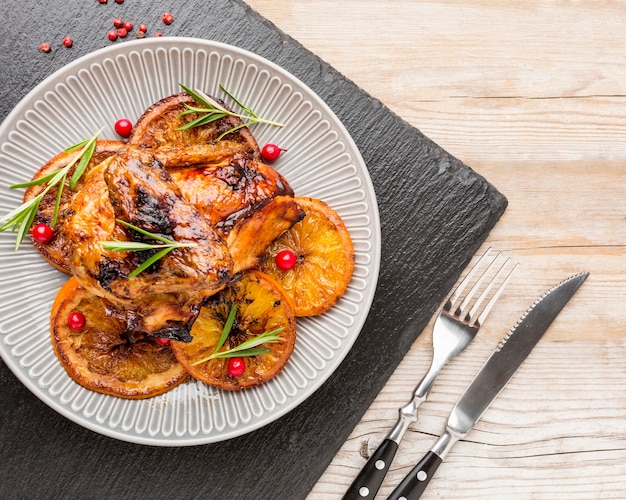 Vista superior de pollo al horno y rodajas de naranja en un plato con cubiertos