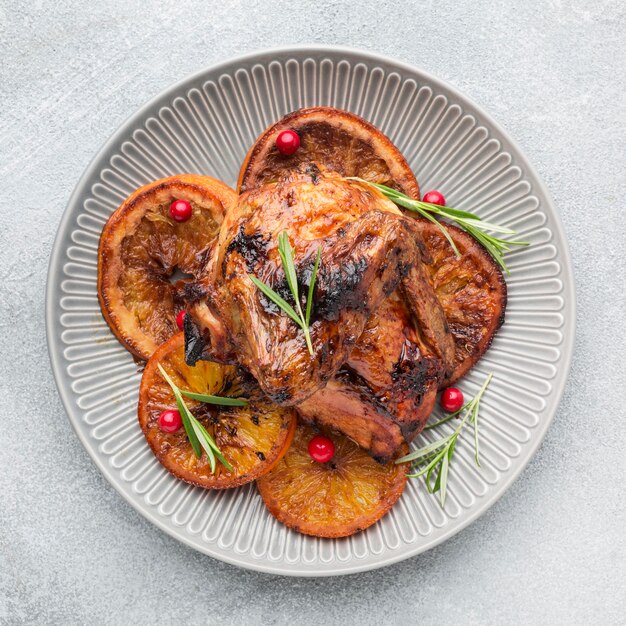 Vista superior de pollo al horno y rodajas de naranja en un plato con hierbas