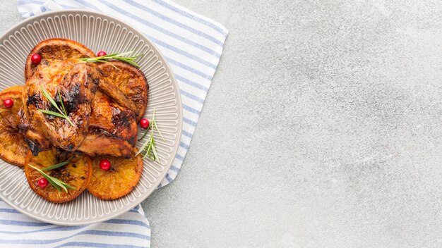 Vista superior de pollo al horno y rodajas de naranja en un plato con un paño de cocina y espacio de copia