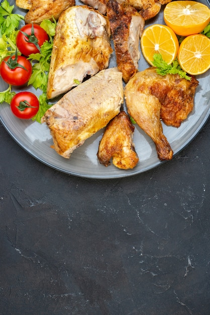 Vista superior de pollo al horno con tomates frescos rodajas de limón en placa en negro