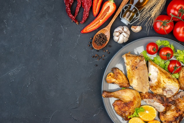 Vista superior de pollo al horno, tomates, rodajas de limón en un plato, pimienta negra, ajo en la mesa