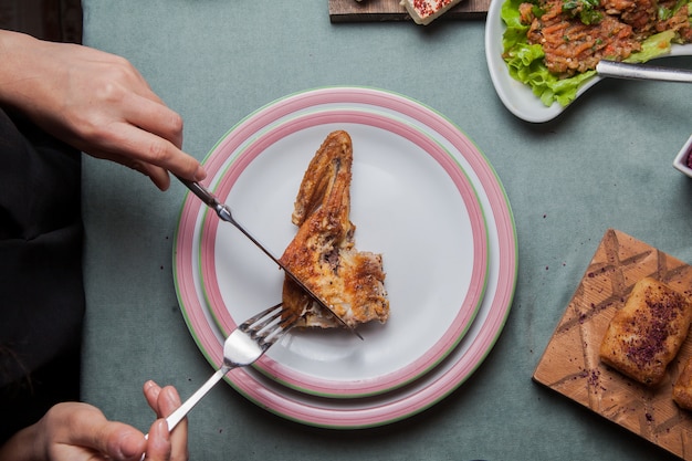 Vista superior de pollo al tabaco en un plato blanco sobre una mesa servida con otra comida, cuchillo, tenedor horizontal