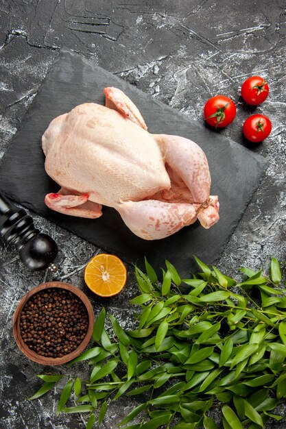 Vista superior pollo crudo fresco con tomates sobre fondo claro-oscuro comida de cocina foto de animal color de carne comida de granja