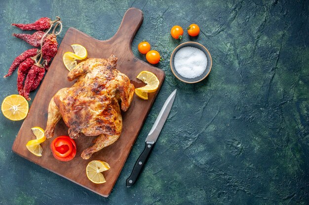 Vista superior de pollo con especias cocidas con rodajas de limón sobre una superficie oscura