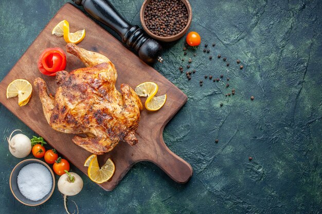 Vista superior de pollo con especias cocidas con rodajas de limón sobre una superficie oscura