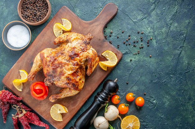 Vista superior de pollo con especias cocidas con rodajas de limón sobre una superficie oscura