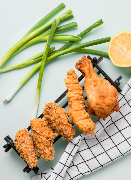 Vista superior de pollo frito en bandeja con cebolla verde, limón y toalla de cocina