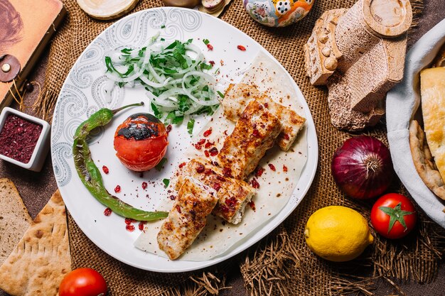 Vista superior de pollo lula kebab en pan de pita con tomate y pimiento asado con cebolla y hierbas