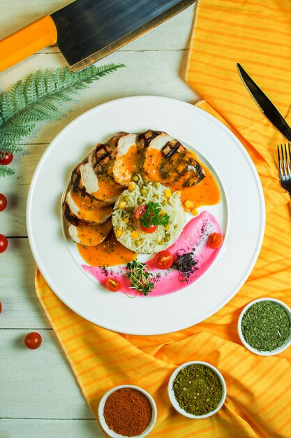 Vista superior de pollo a la parrilla con arroz mezclado con guisantes y cornon un plato blanco