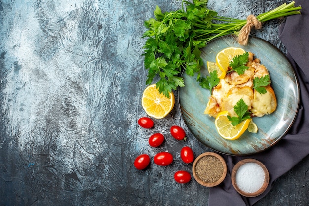 Vista superior de pollo con queso en plato manojo de perejil limón tomates cherry especias en tazones sobre mesa gris con lugar de copia