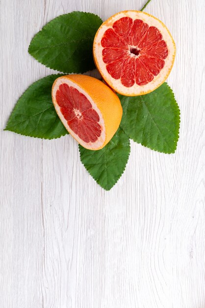 Una vista superior de pomelo en rodajas frescas con hojas verdes sobre blanco, jugo de cítricos