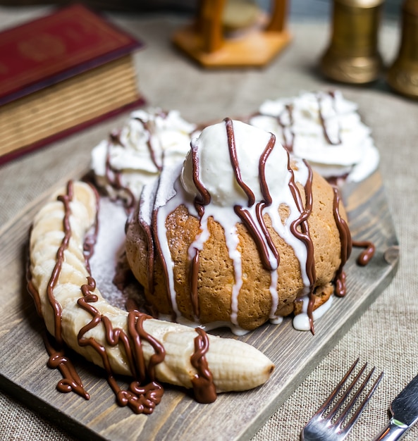 Vista superior de postre con helado y crema batida adornada con rodajas de plátano y chocolate vertido en el tablero