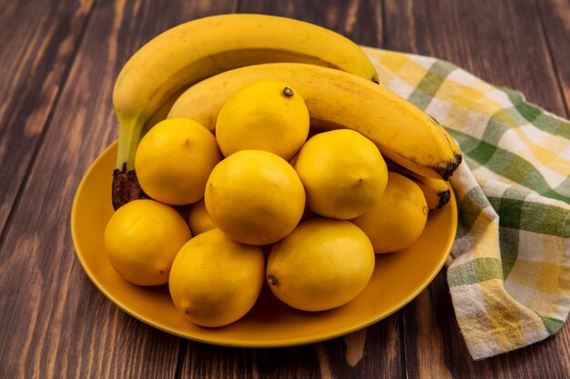 Vista superior de potentes limones antioxidantes en una placa amarilla sobre una tela marcada con plátanos sobre una superficie de madera