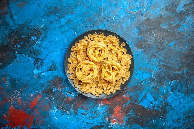 Vista superior de la preparación de la cena con fideos de pasta en una placa negra sobre fondo azul.