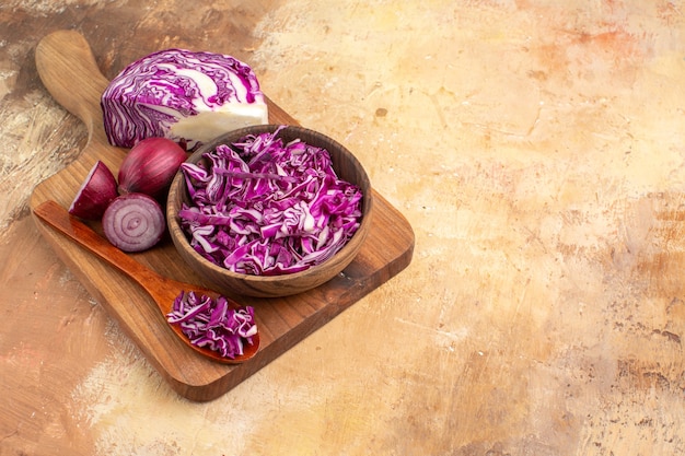 Vista superior de la preparación de ensalada de verduras frescas con repollo rojo y cebollas en una tabla de cortar sobre una mesa de madera con espacio de copia