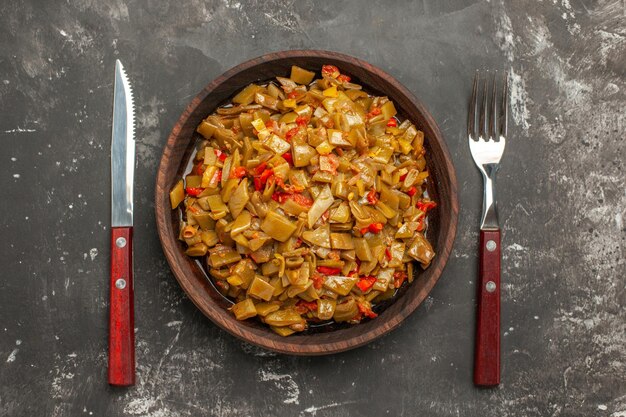Vista superior de primer plano apetitoso plato apetitoso plato de judías verdes con tomates entre tenedor y cuchillo en la mesa oscura