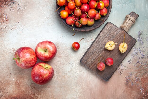 Vista superior de primer plano cerezas ramas de árboles cerezas en el recipiente y en el tablero tres manzanas