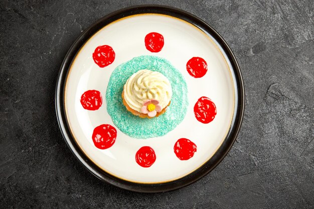 Vista superior de primer plano cupcake cupcake apetitoso con salsa roja en el plato blanco en el centro de la mesa negra