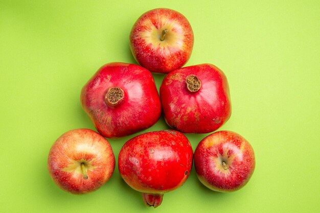 Vista superior de primer plano frutas las apetitosas granadas y tres manzanas rojas en la superficie verde