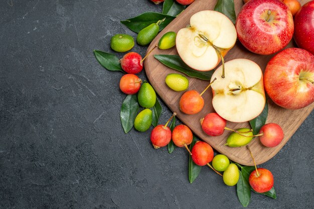 Vista superior de primer plano frutas cerezas manzanas con hojas cítricos en la tabla de cortar