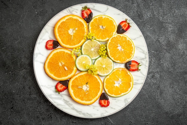 Vista superior de primer plano naranja en rodajas de naranja limón y fresas cubiertas de chocolate en un plato blanco en el centro de la mesa