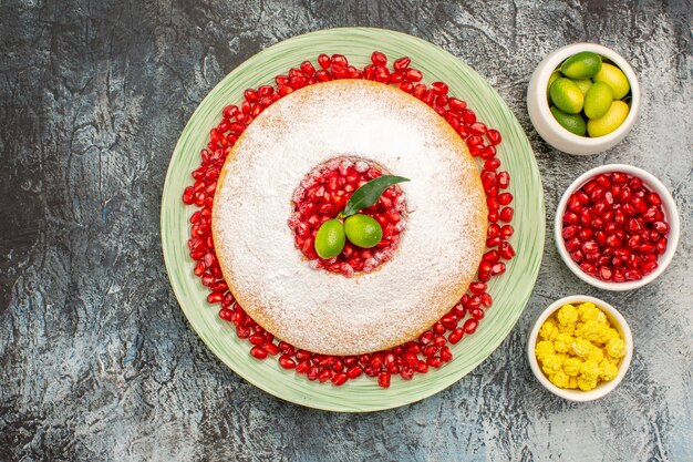 Vista superior de primer plano pastel y dulces un plato de pastel con tazones de granada de caramelos de frutas cítricas