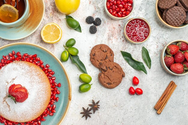 Vista superior de primer plano pastel de fresa plato de pastel de fresas y semillas de granada una taza de té galletas de frutas cítricas anís estrellado sobre la mesa