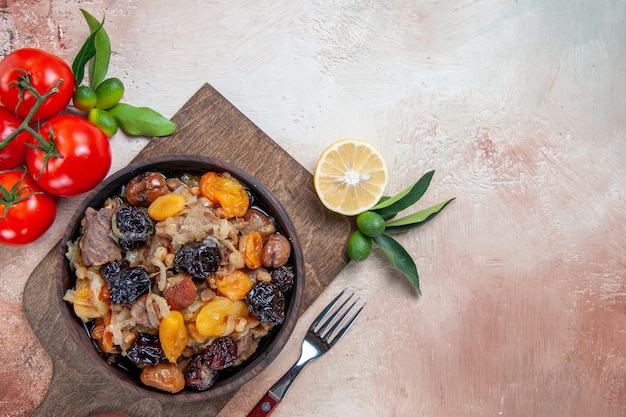 Foto gratuita vista superior de primer plano pilaf pilaf con frutos secos en el tablero tenedor tomates limón