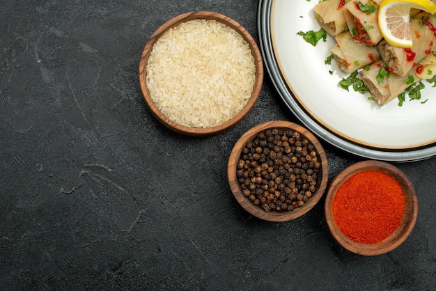 Vista superior de primer plano plato blanco de repollo relleno con hierbas limón y salsa en un plato blanco y cuencos de especias coloridas, pimienta negra y arroz en la mesa