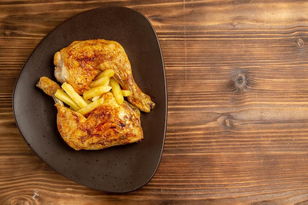 Vista superior de primer plano plato de comida rápida de papas fritas y patas de pollo en el lado izquierdo de la mesa de madera