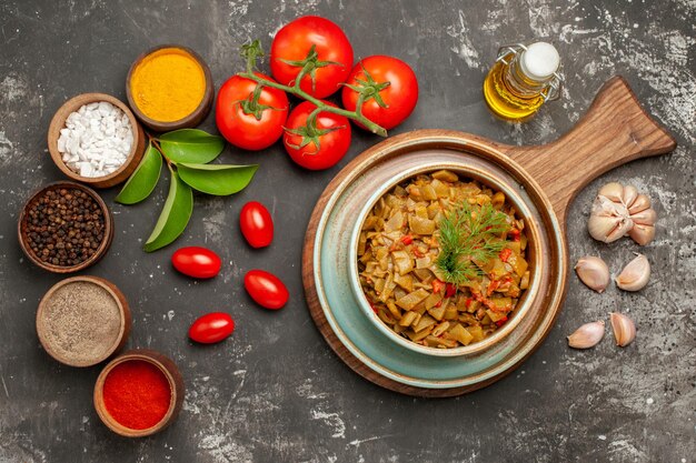 Vista superior de primer plano plato de especias de judías verdes cuencos de ajo de especias coloridas hojas de tomates con pedicelos botella de aceite sobre la mesa oscura