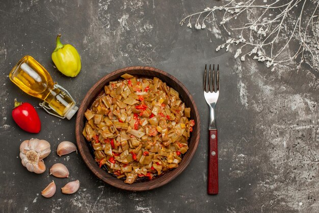 Vista superior de primer plano plato de frijoles pimientos botella de aceite de ajo junto al tenedor y plato de judías verdes y tomates en la mesa