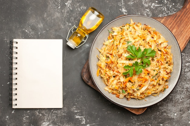 Vista superior de primer plano repollo plato de repollo en la tabla de cortar botella de aceite cuaderno blanco