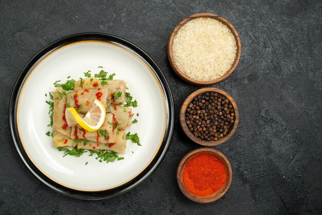 Vista superior de primer plano repollo relleno repollo relleno con hierbas de limón y salsa y tazones de arroz especias coloridas y pimienta negra sobre mesa negra