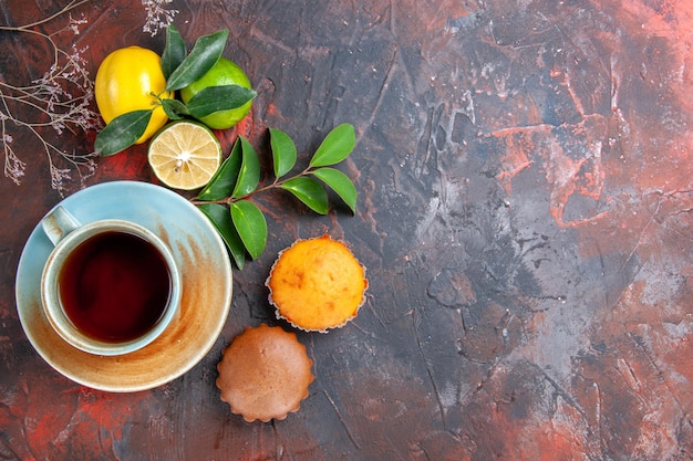 Vista superior de primer plano una taza de té una taza de té en el platillo frutas cítricas con cupcakes de hojas