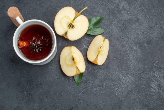 Vista superior de primer plano una taza de té una taza de té con ramas de canela junto a las rodajas de manzana