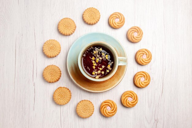 Vista superior de primer plano té con galletas taza blanca de té de hierbas y apetitosas galletas a su alrededor en la mesa blanca