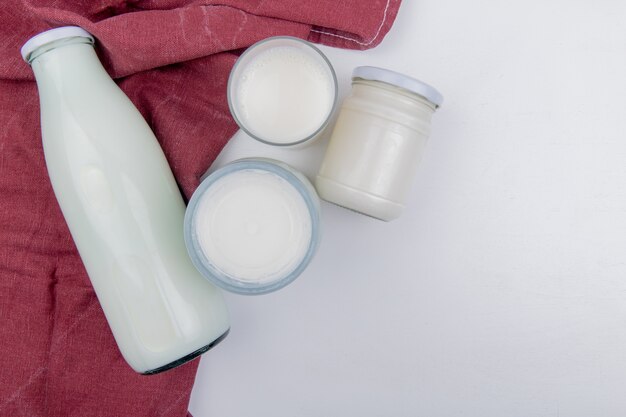 Vista superior de productos lácteos como leche agria, leche coagulada y crema sobre tela bordo y fondo blanco con espacio de copia