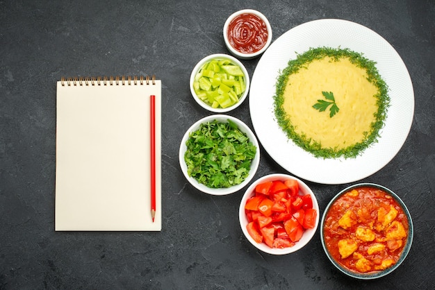 Vista superior de puré de patatas con verduras y tomates en gris