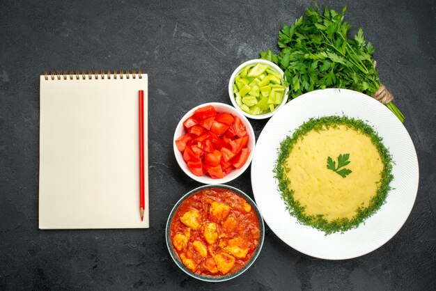 Vista superior de puré de patatas con verduras y tomates en rodajas en gris