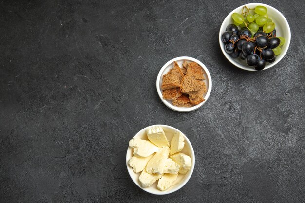 Vista superior de queso blanco con uvas frescas en superficie oscura, comida de frutas, comida de leche, pan